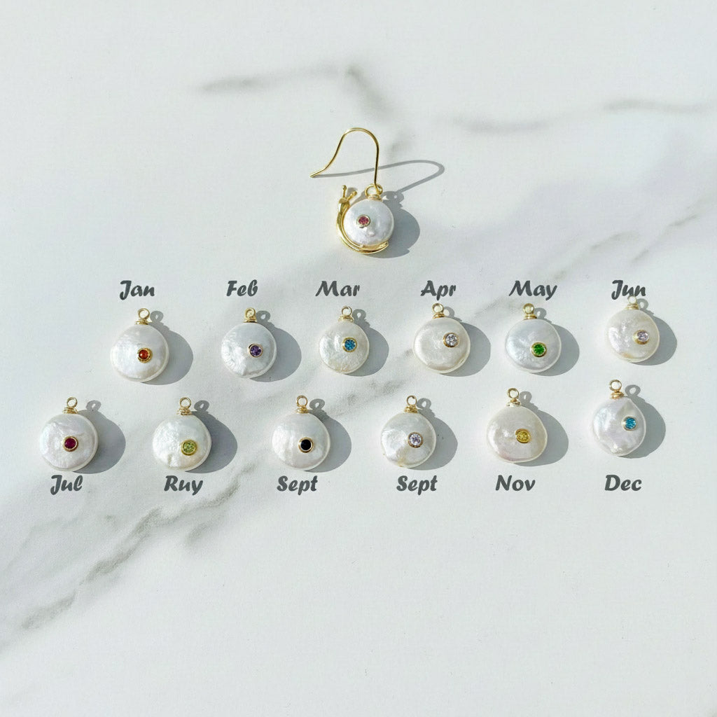 Set of pearl earrings with colorful gemstones, each labeled for a month on a marble background.