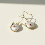 Gold earrings with pearl-like stones on a light beige background