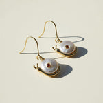 Snail-shaped earrings with pearl shells and gold accents on a beige background
