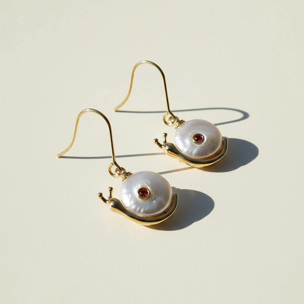 Snail-shaped earrings with pearl shells and gold accents on a beige background