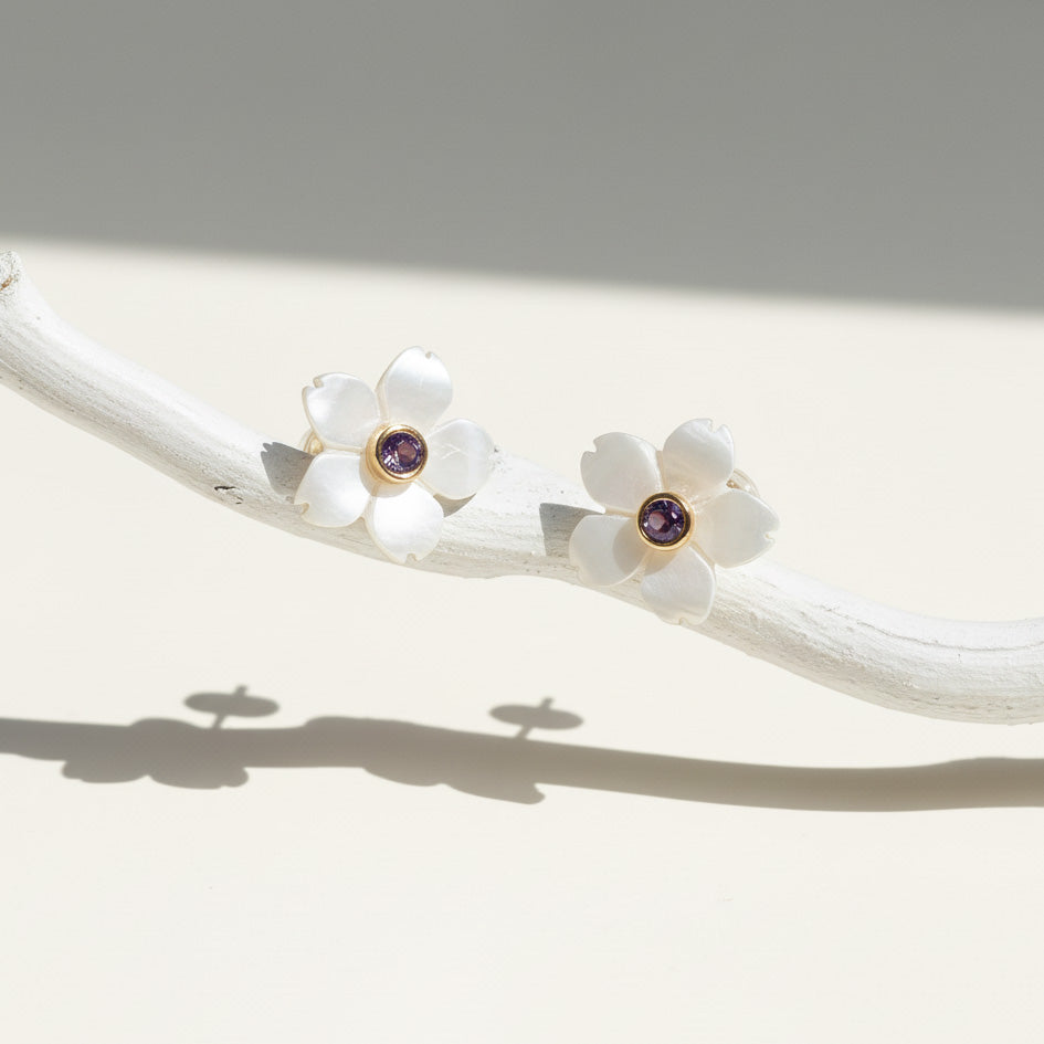 Pair of white flower earrings with purple gemstones on a white branch.