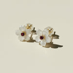 Flower-shaped earrings with red gemstones on a beige background