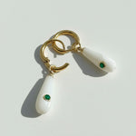 Gold and white earrings with green gemstones on a light gray background