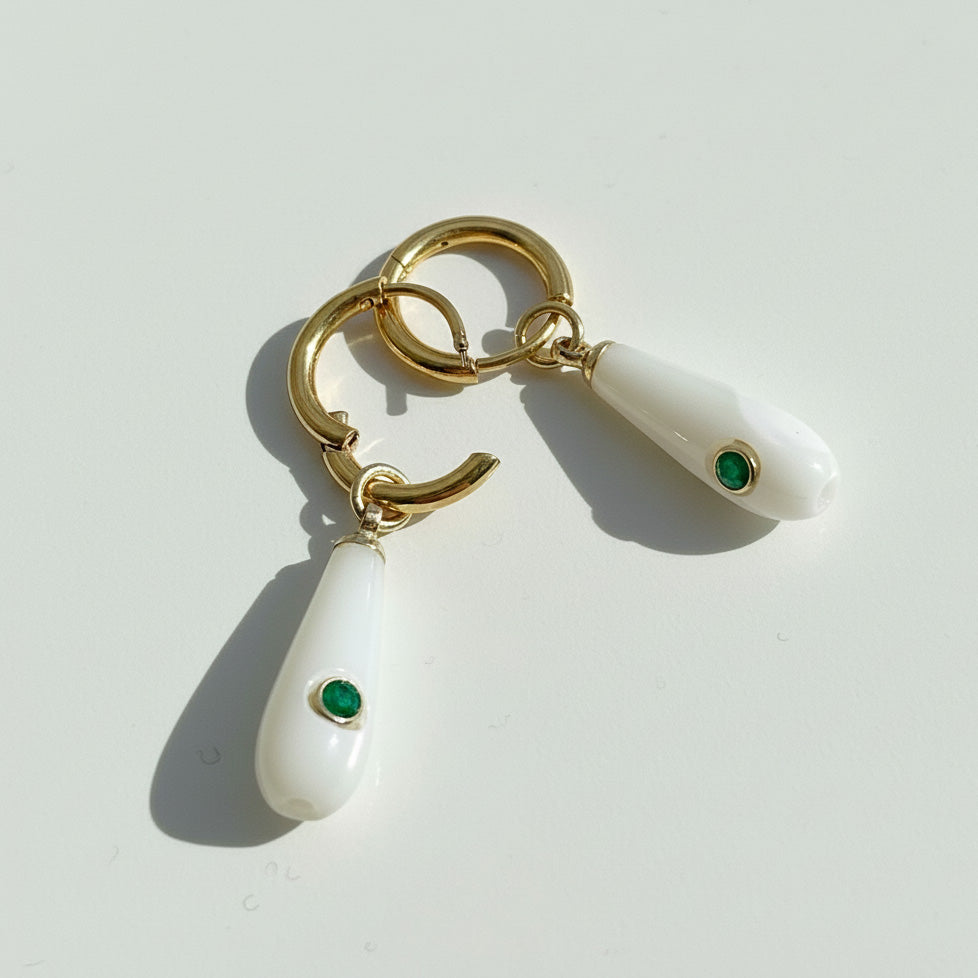 Gold and white earrings with green gemstones on a light gray background