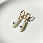 Gold earrings with white stones and purple gemstones on a light background