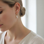 Close-up of a woman wearing a gold earring with a pearl-like bead.