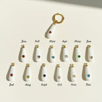 Teardrop-shaped charms with gemstones for each month on a beige background