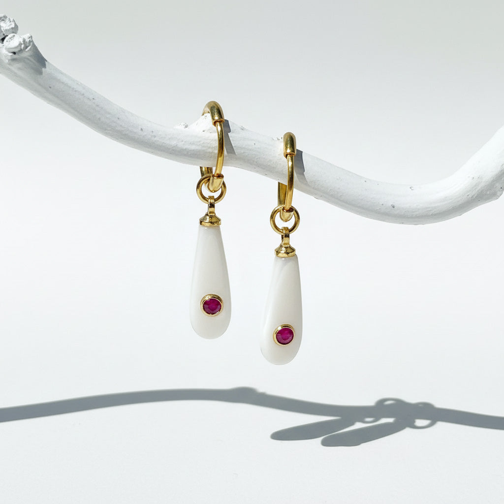 Pair of earrings with gold hooks, white teardrop-shaped stones, and red gemstones on a white background.