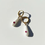 Pair of earrings with gold loops and teardrop-shaped white stones on a light gray background
