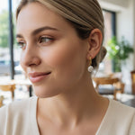 Woman wearing gold and pearl earrings in a blurred indoor setting