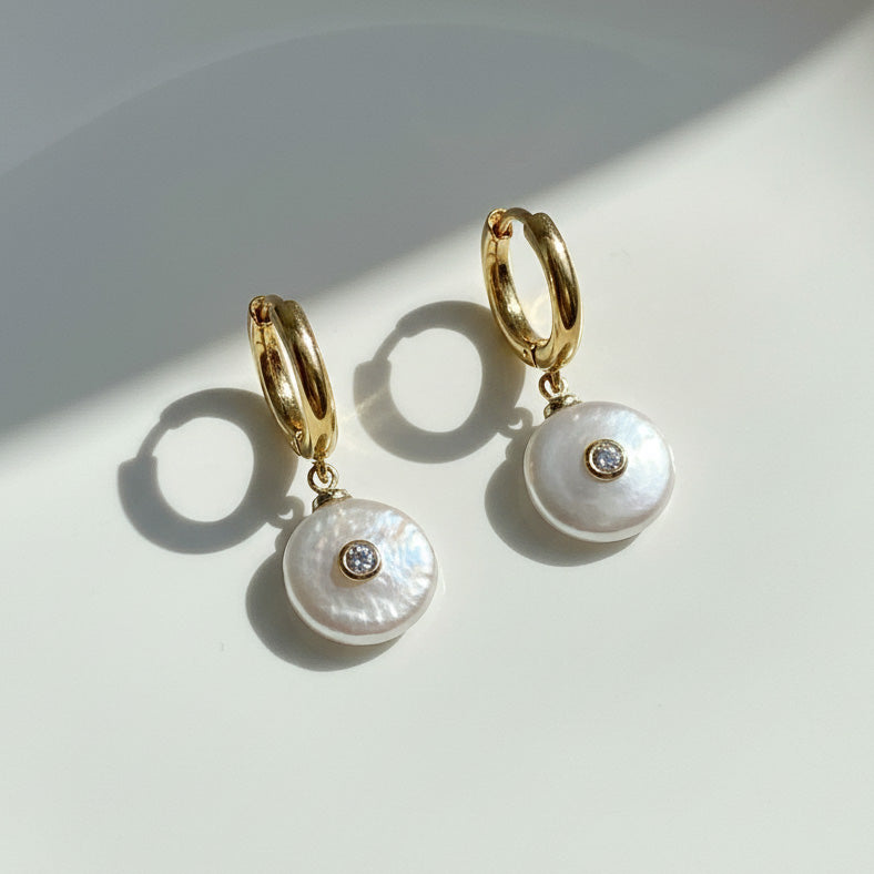 Gold hoop earrings with pearl drops on a light background