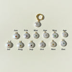 Pearl charms with gemstones labeled for each month on a light background