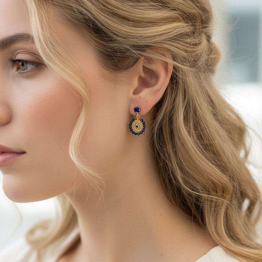 Woman wearing gold and navy blue beaded dangle earrings with intricate circular woven design.