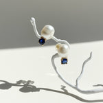 Pearl earrings with blue gemstones on a white branch against a gray background
