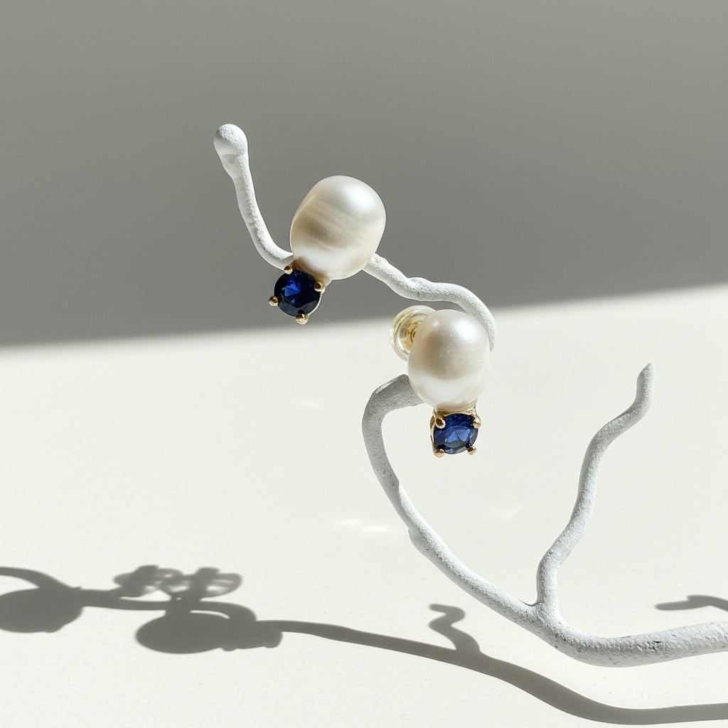Pearl earrings with blue gemstones on a white branch against a gray background