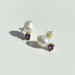 Pearl earrings with purple gemstones on a light gray background