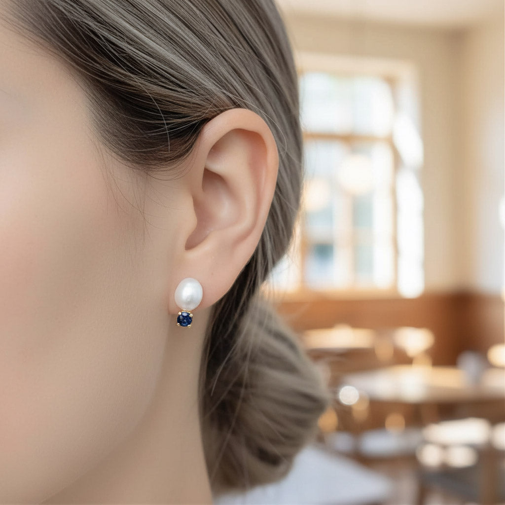 Pearl earring with a blue gemstone worn by a person indoors.
