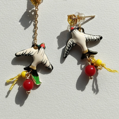 Pair of earrings with bird design and colorful beads on a light gray background