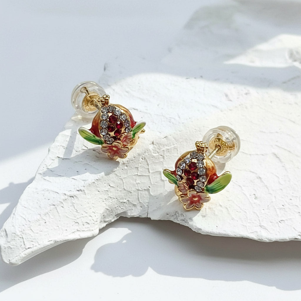 Red and green enamel pomegranate earrings on white stone.