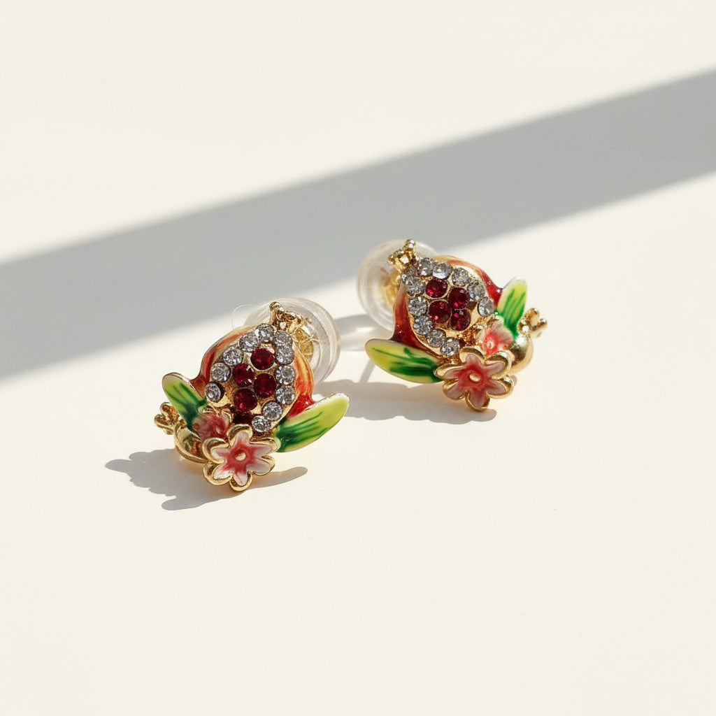 Hand-painted pomegranate enamel stud earrings with crystals on cream background.