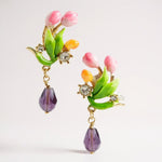 Colorful floral earrings with green leaves and purple beads on a light gray background