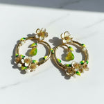 Gold hoop earrings with floral and green accents on a white background