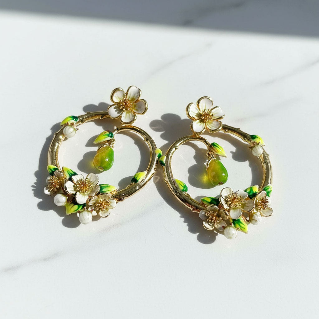 Gold hoop earrings with floral and green accents on a white background