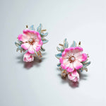 Pair of floral earrings with pink flowers and gold accents on a light gray background
