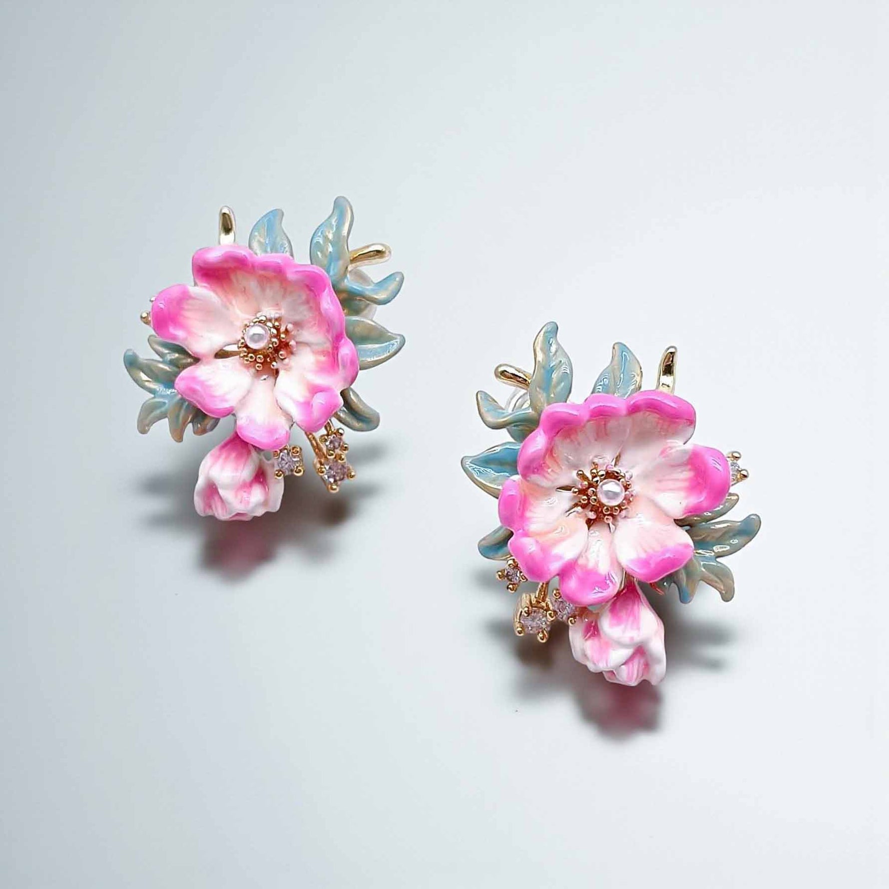 Pair of floral earrings with pink flowers and gold accents on a light gray background