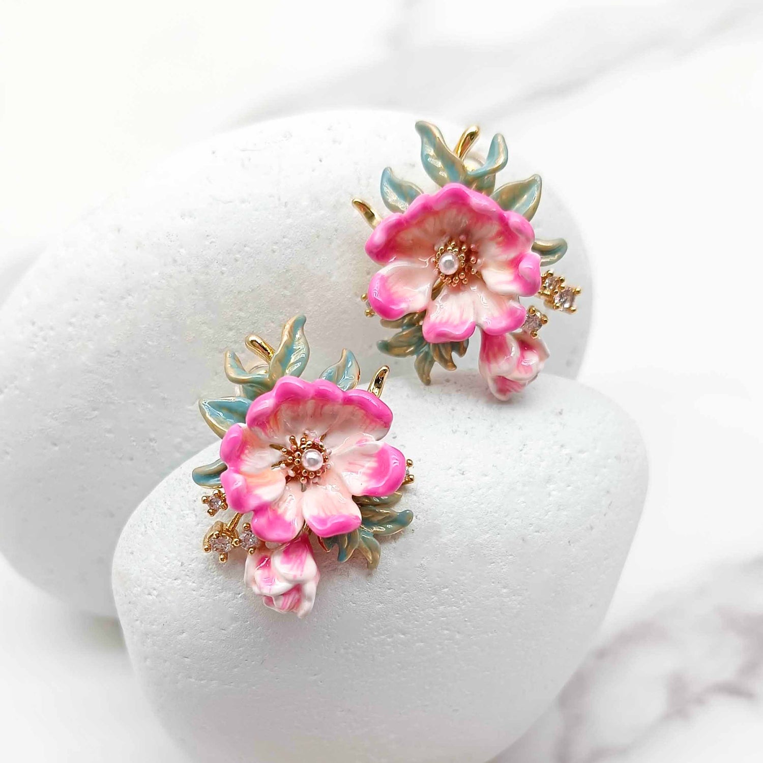 Pair of pink floral earrings on a white stand with a white background