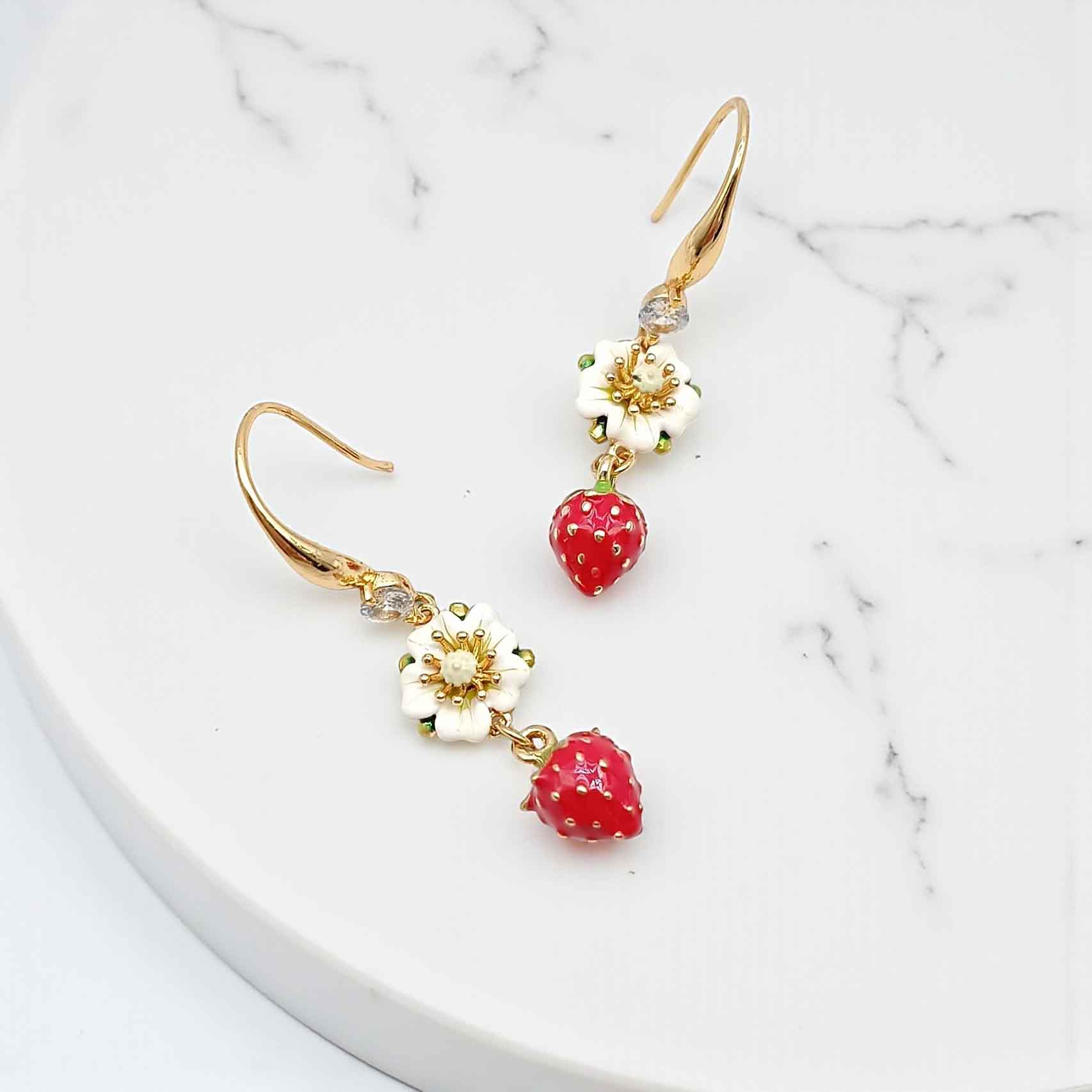 Gold earrings with red berry-like charms on a marble surface