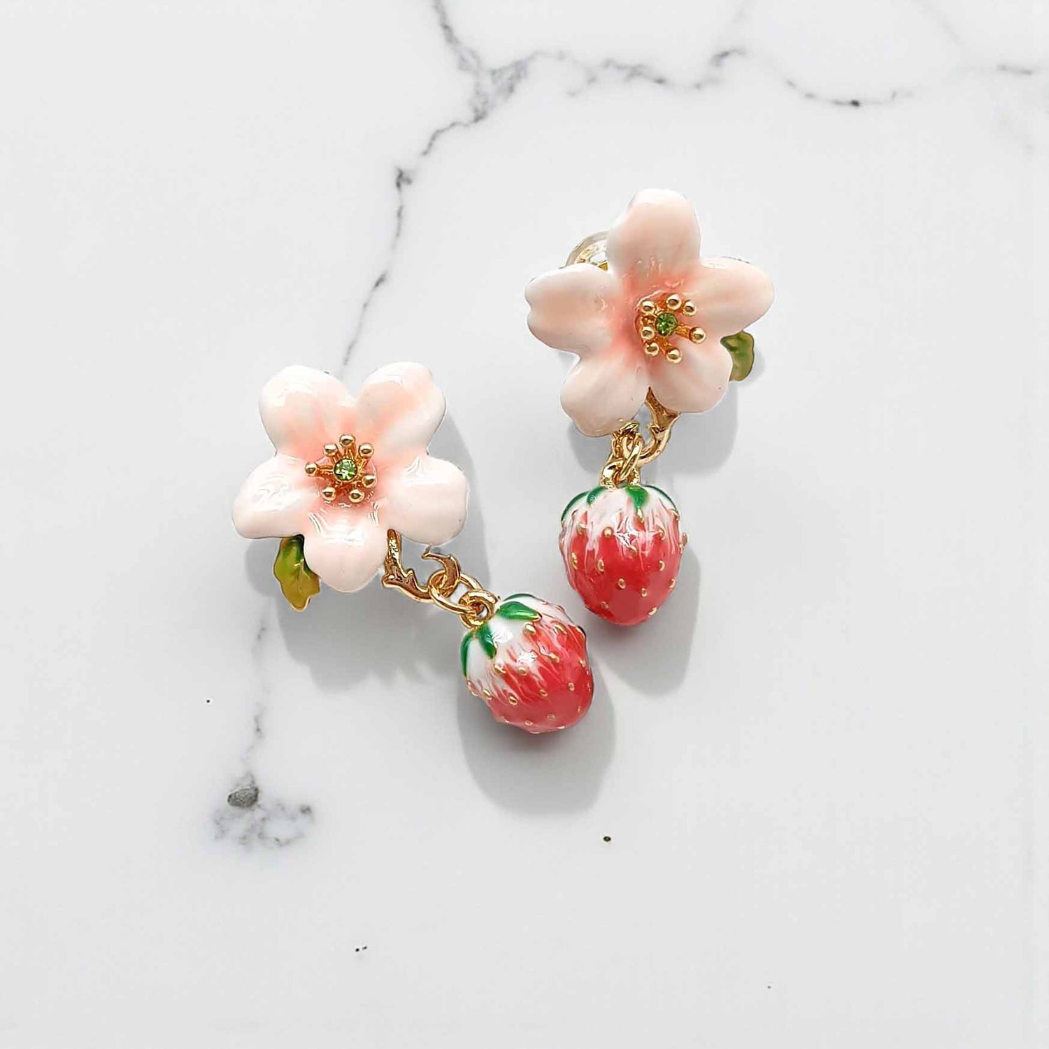Floral and strawberry-themed earrings on a marble background