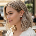 “Model wearing a handcrafted strawberry-themed earring featuring a pink flower stud and dangling red strawberry charm, photographed outdoors in natural light