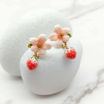 Floral and strawberry-themed earrings on a white stand with a marble background