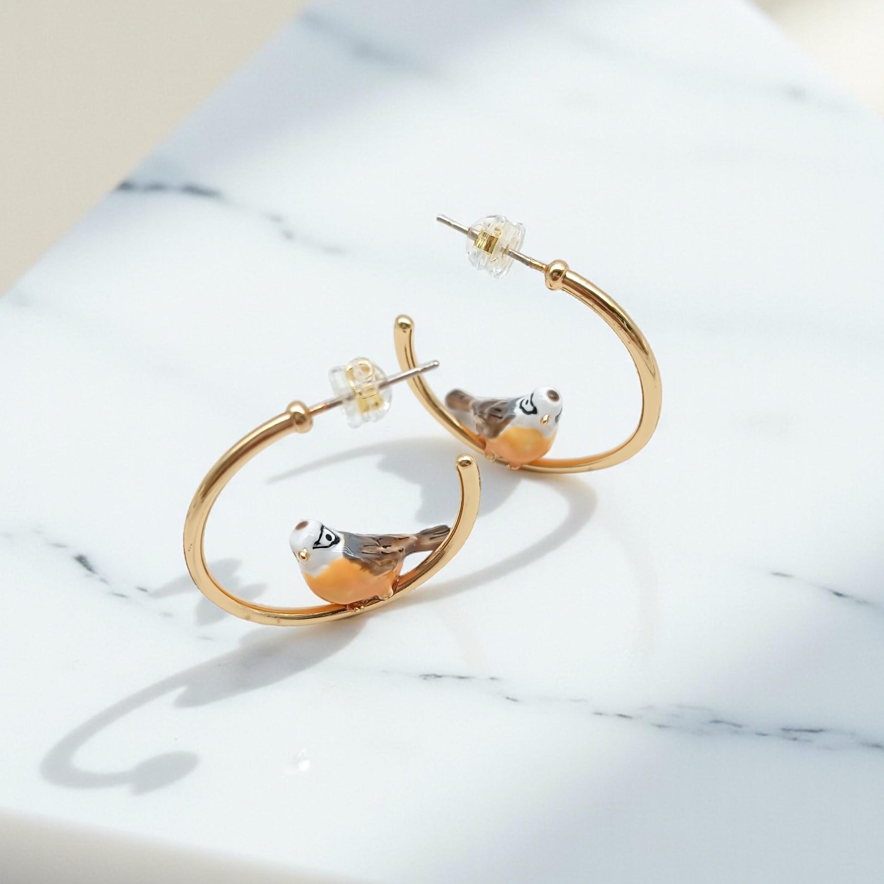 Gold hoop earrings with bird designs on a marble surface