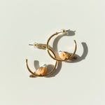 Gold hoop earrings with peach-colored stones on a light beige background
