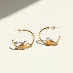 Gold hoop earrings with bird designs on a beige background