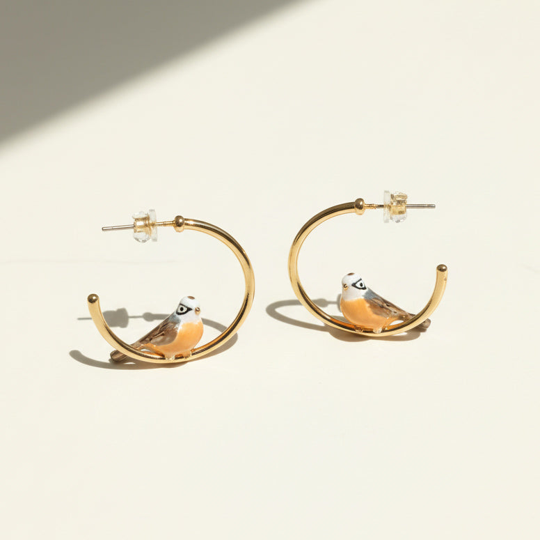 Gold hoop earrings with bird designs on a beige background