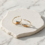 Gold hoop earrings with bird designs on a textured stone surface.