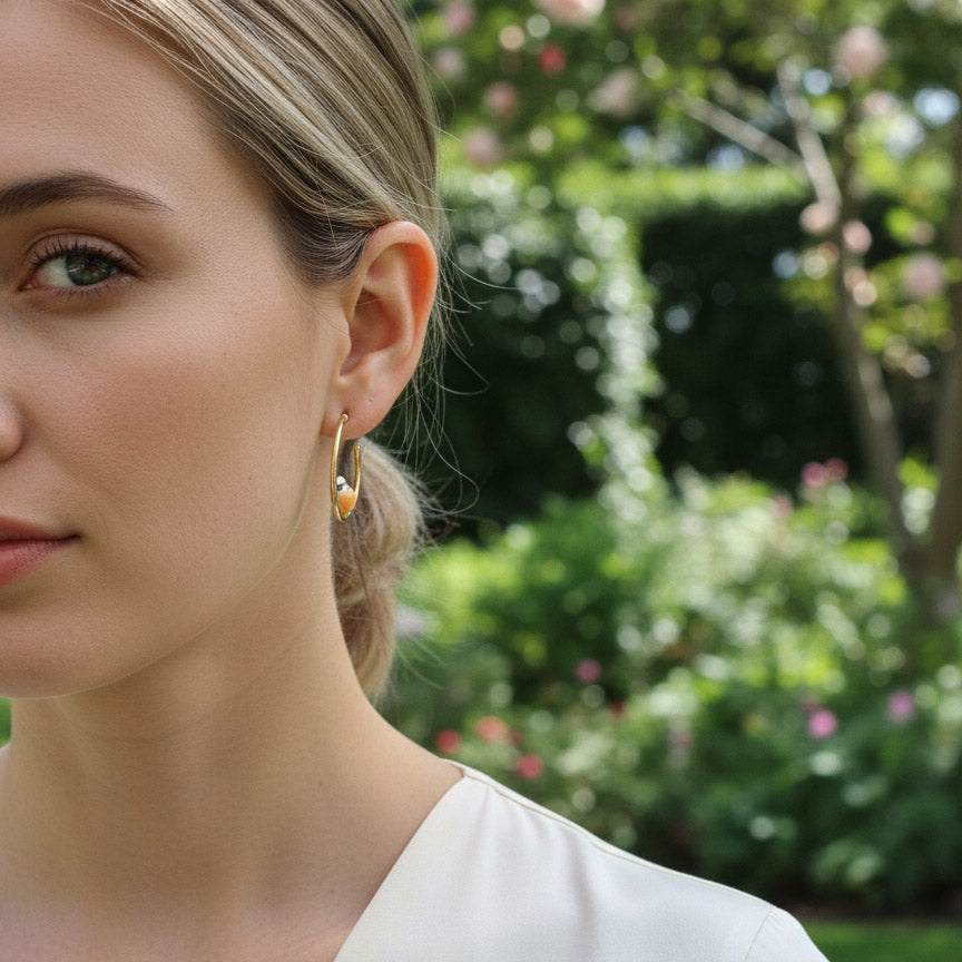 Close-up of a woman wearing gold hoop earrings with a blurred garden background