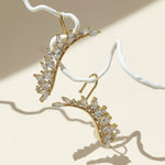 Gold earrings with clear gemstones on a beige background