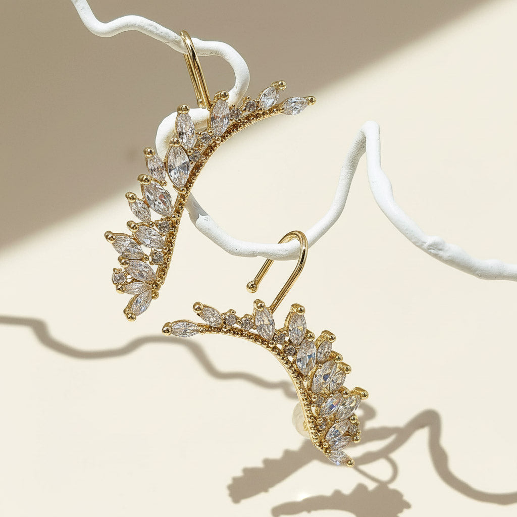 Gold earrings with clear gemstones on a beige background