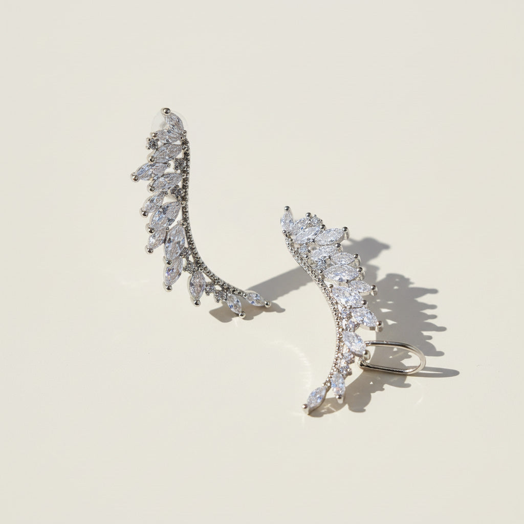 Silver leaf-shaped earrings with clear stones on a beige background
