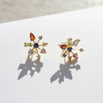 Gold plated multicolour CZ starburst stud earrings photographed in sunlight on white surface.