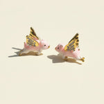 Two pink pig figurines with gold wings on a beige background