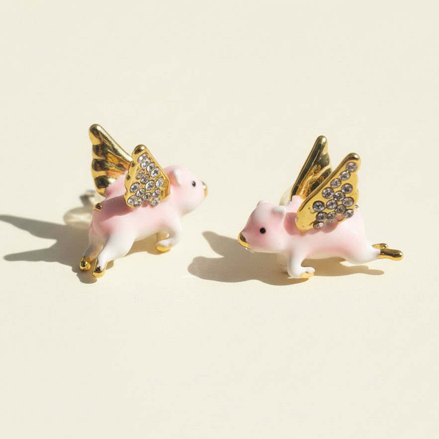 Pair of pink pig earrings with gold wings on a beige background