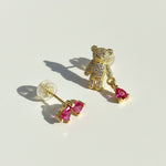 Gold teddy bear earrings with pink gemstones on a light background