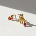 Gold teddy bear-shaped earring with pink gemstones on a white surface