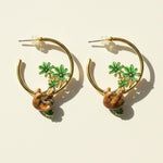Gold hoop earrings with sloth and palm tree designs on a beige background