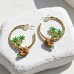 Gold hoop earrings with sloth and tree  designs on a white stone surface